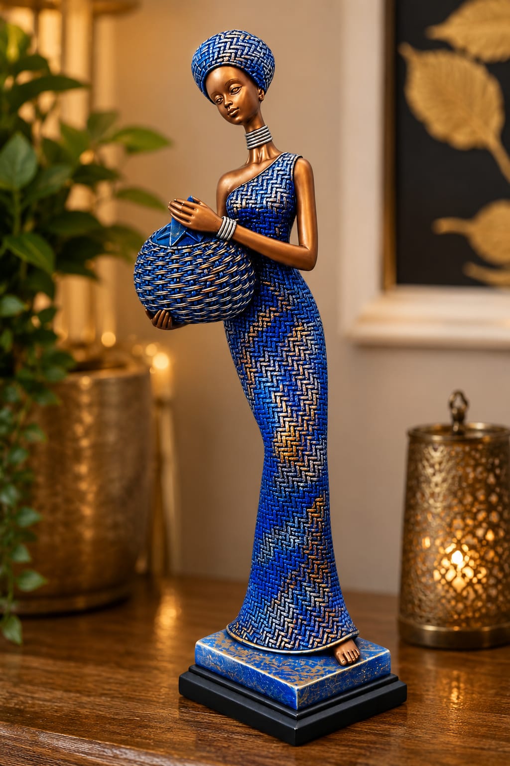 A decorative figurine of a woman in a blue and gold chevron-patterned dress and matching headwrap, holding a matching basket, displayed on a wooden surface in a warmly lit indoor setting.
