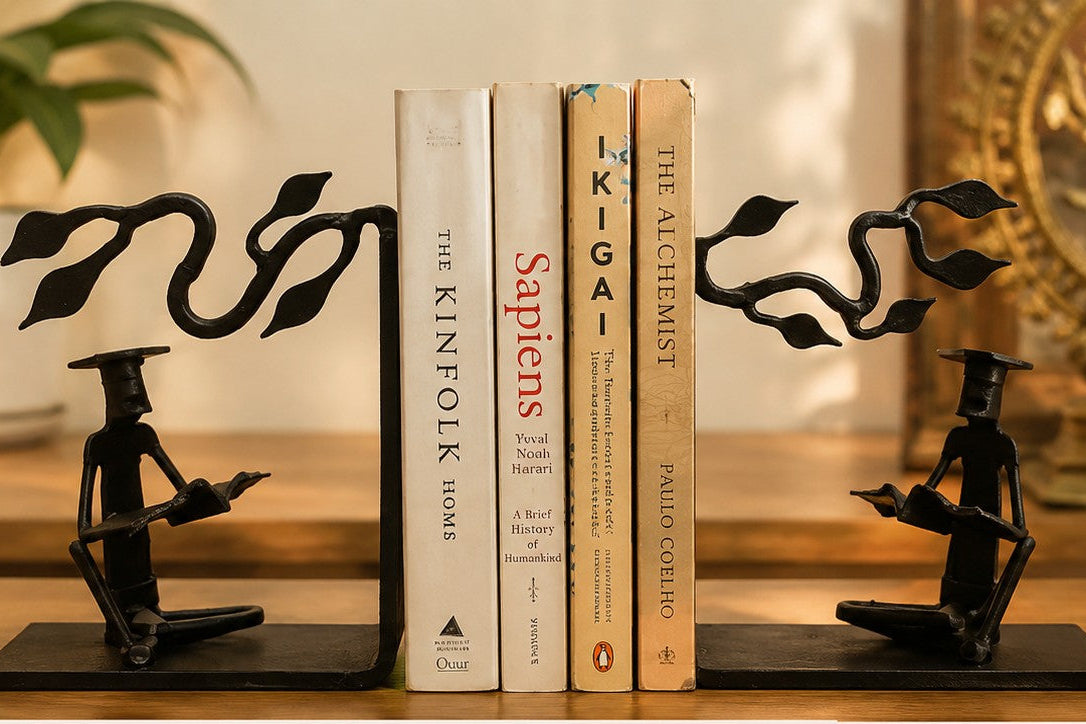 Black metal bookends shaped like seated figures holding a quill, displayed on a shelf holding four books between them.